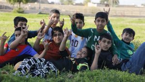 A group of smiling boys outdoors, raising their hands in playful gestures during a Dana Energy Idano Project activity, part of Dana Energy’s CSR initiatives in Iran that promote education, creativity, and community engagement.